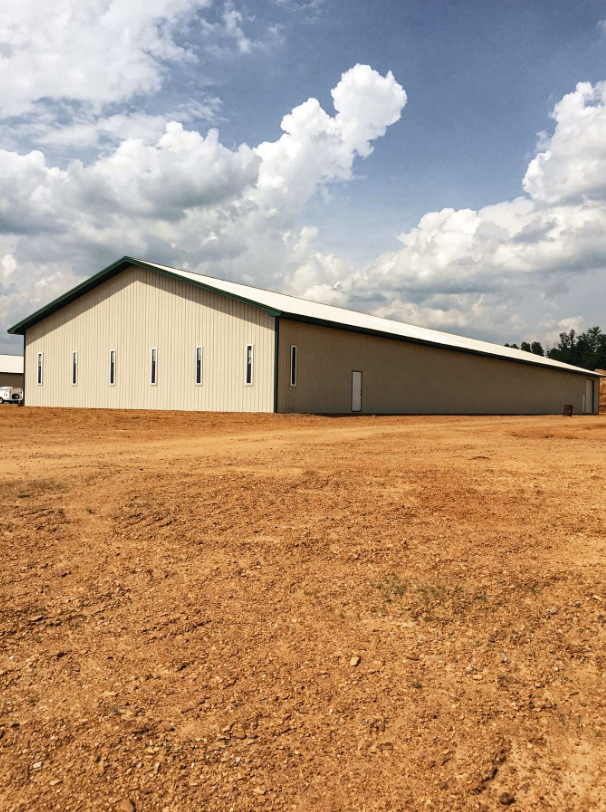 Gray metal building with a large porch; red ladder leaning against it on a dirt lot under a blue sky.