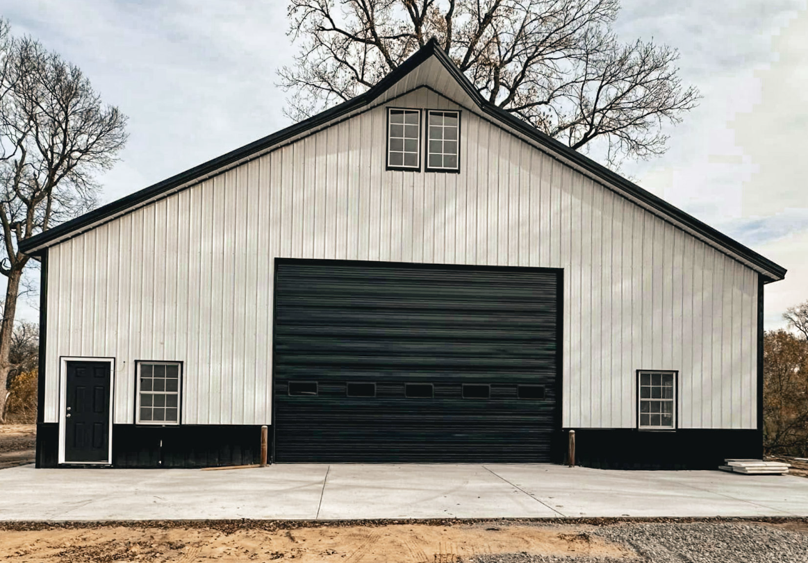 Tan and black two-car garage with black roof and white garage doors; set in a field with trees in the background.