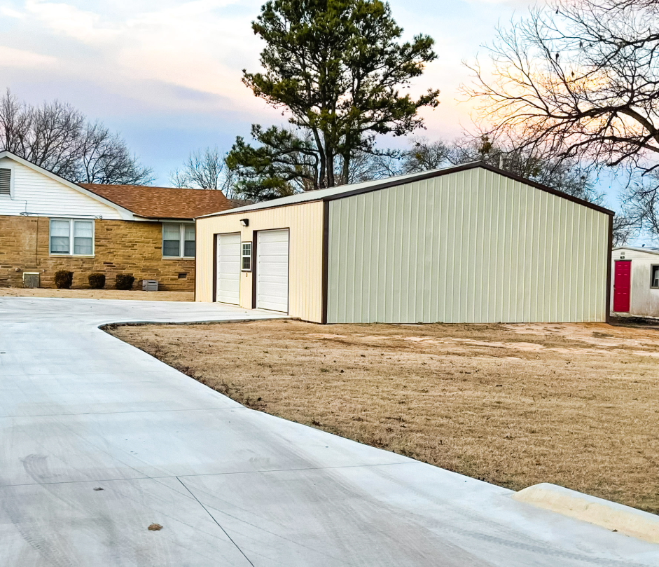 White and black metal farm shed with a red tractor inside. Overcast day.