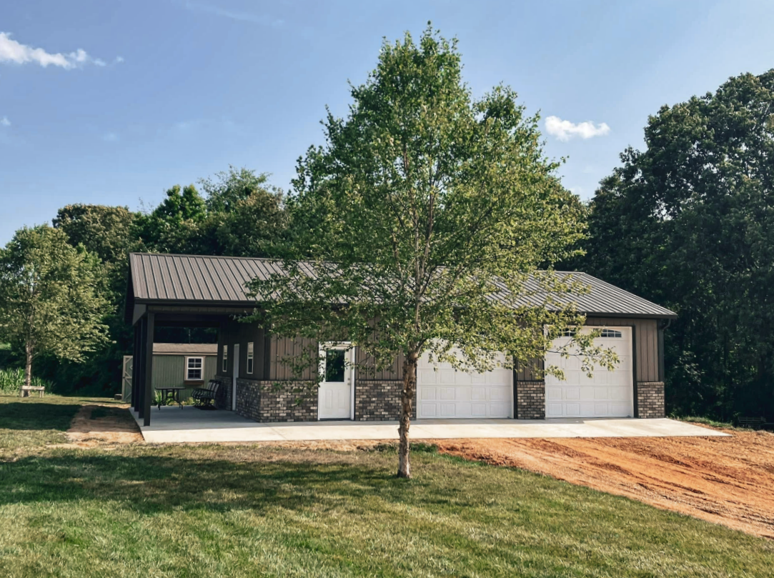 White and brown metal building with garage door, bare tree in background, sunny day.