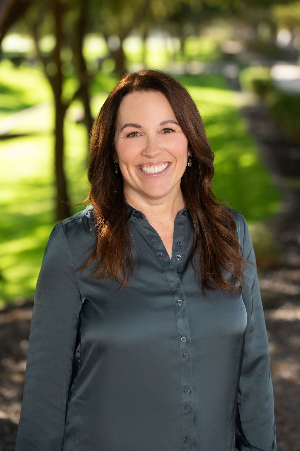 A woman in a blue shirt is smiling for the camera in a park.
