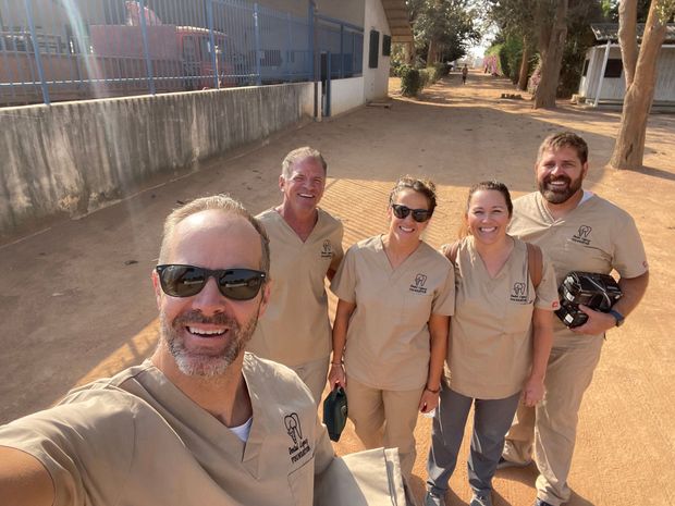 A group of people wearing scrubs and sunglasses are posing for a picture.