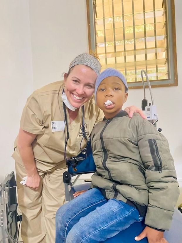 A nurse is posing for a picture with a young boy sitting in a chair.