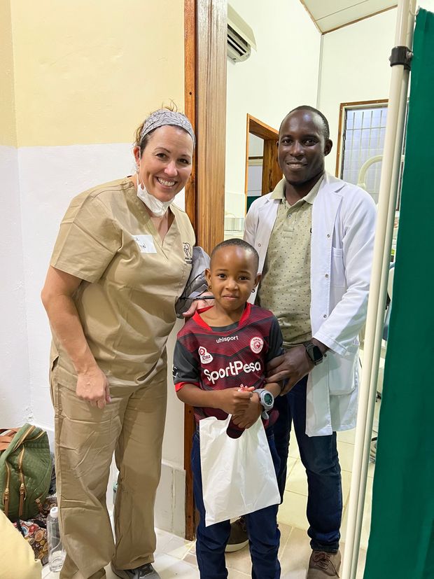 A doctor and a nurse are posing for a picture with a young boy in a hospital room.