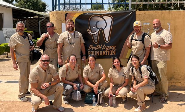 A group of people are posing for a picture in front of a sign that says dental legacy foundation.