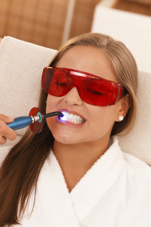 A woman wearing red sunglasses is getting her teeth whitened