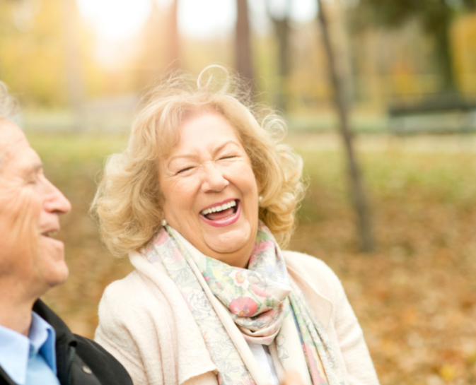 An elderly couple is laughing together in a park.