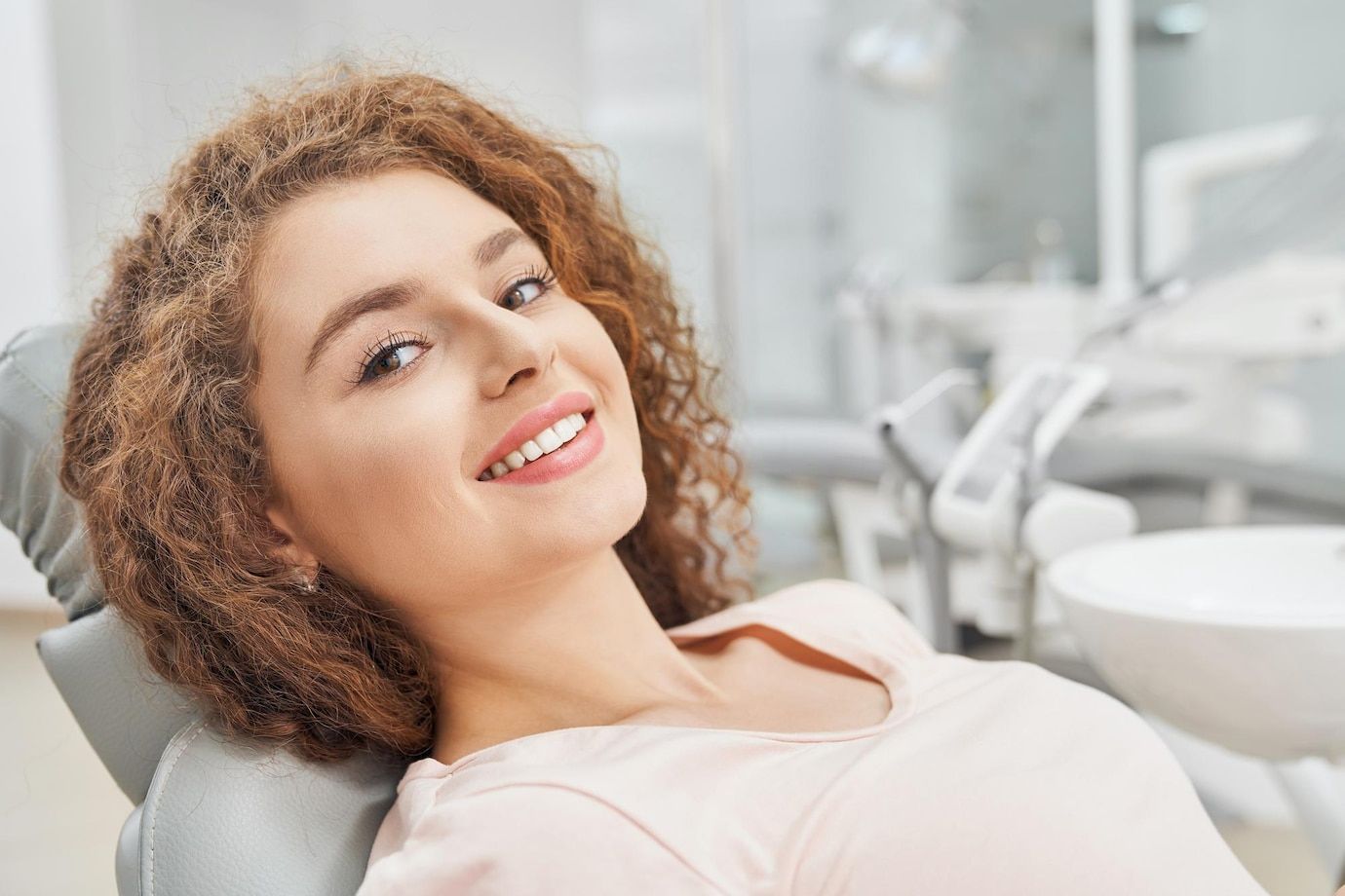 A woman is smiling while sitting in a dental chair.