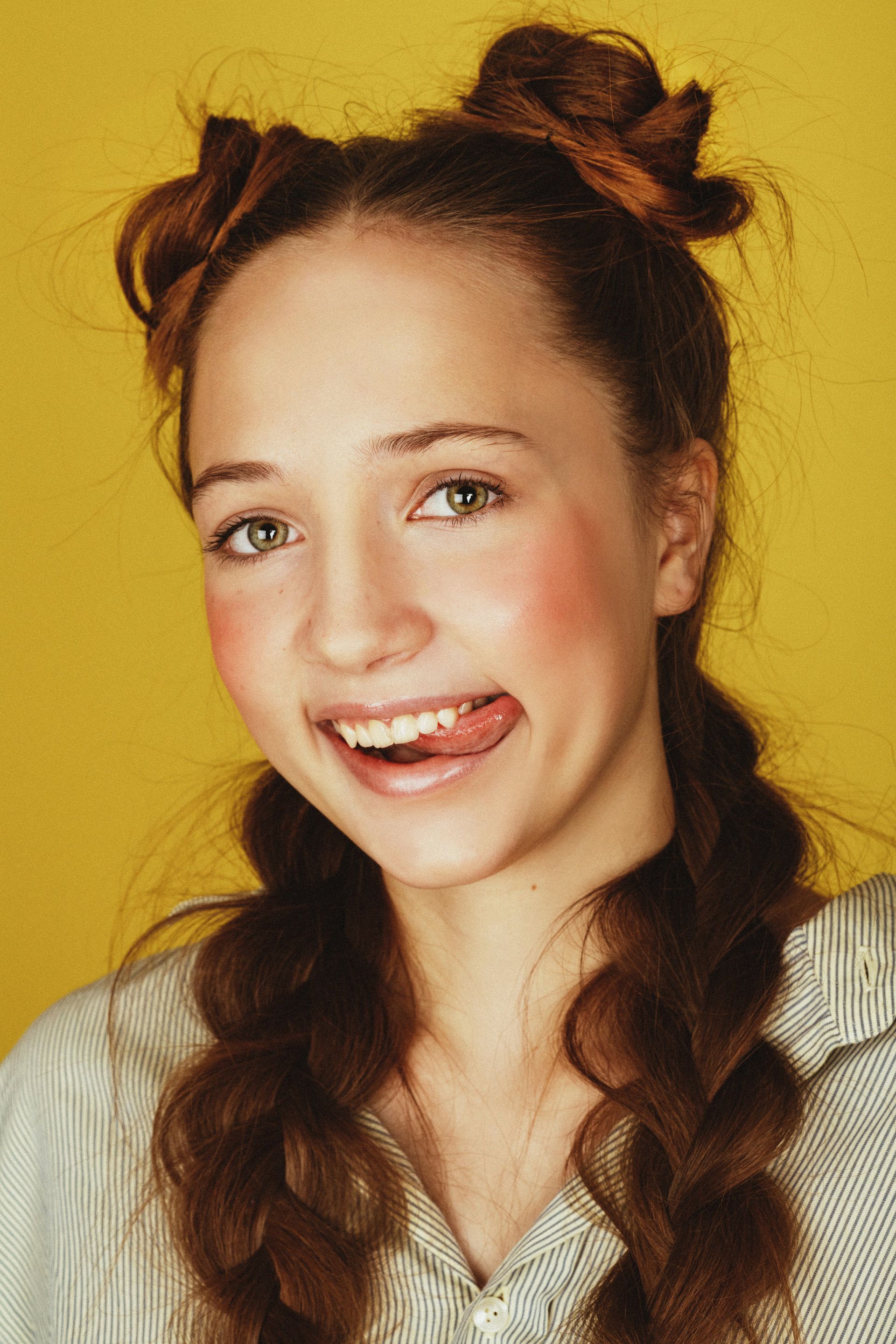 A young woman with two braids in her hair is smiling and sticking her tongue out.