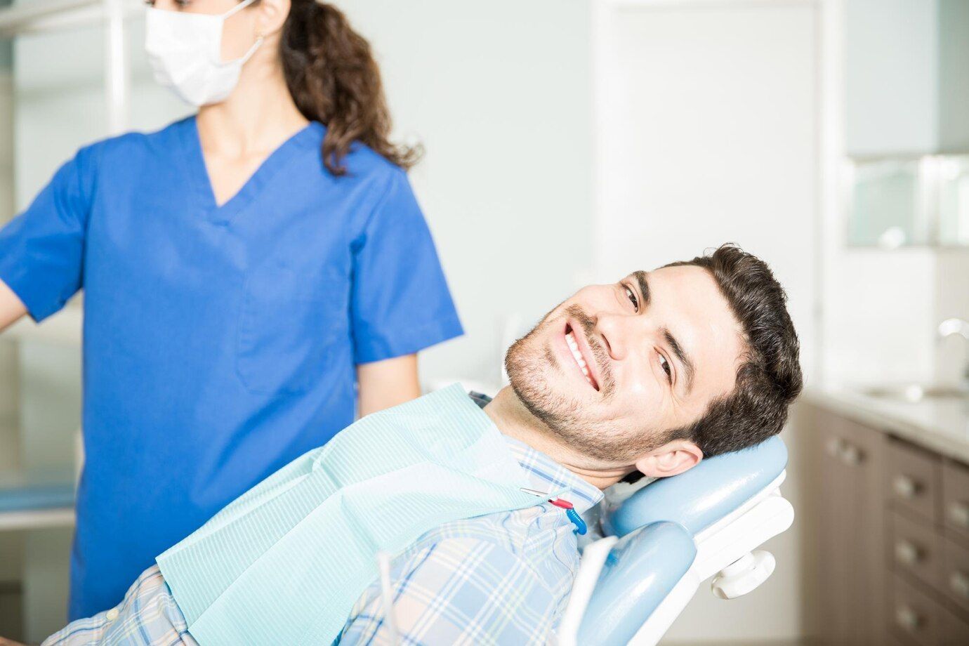 A man is sitting in a dental chair with a nurse standing behind him.