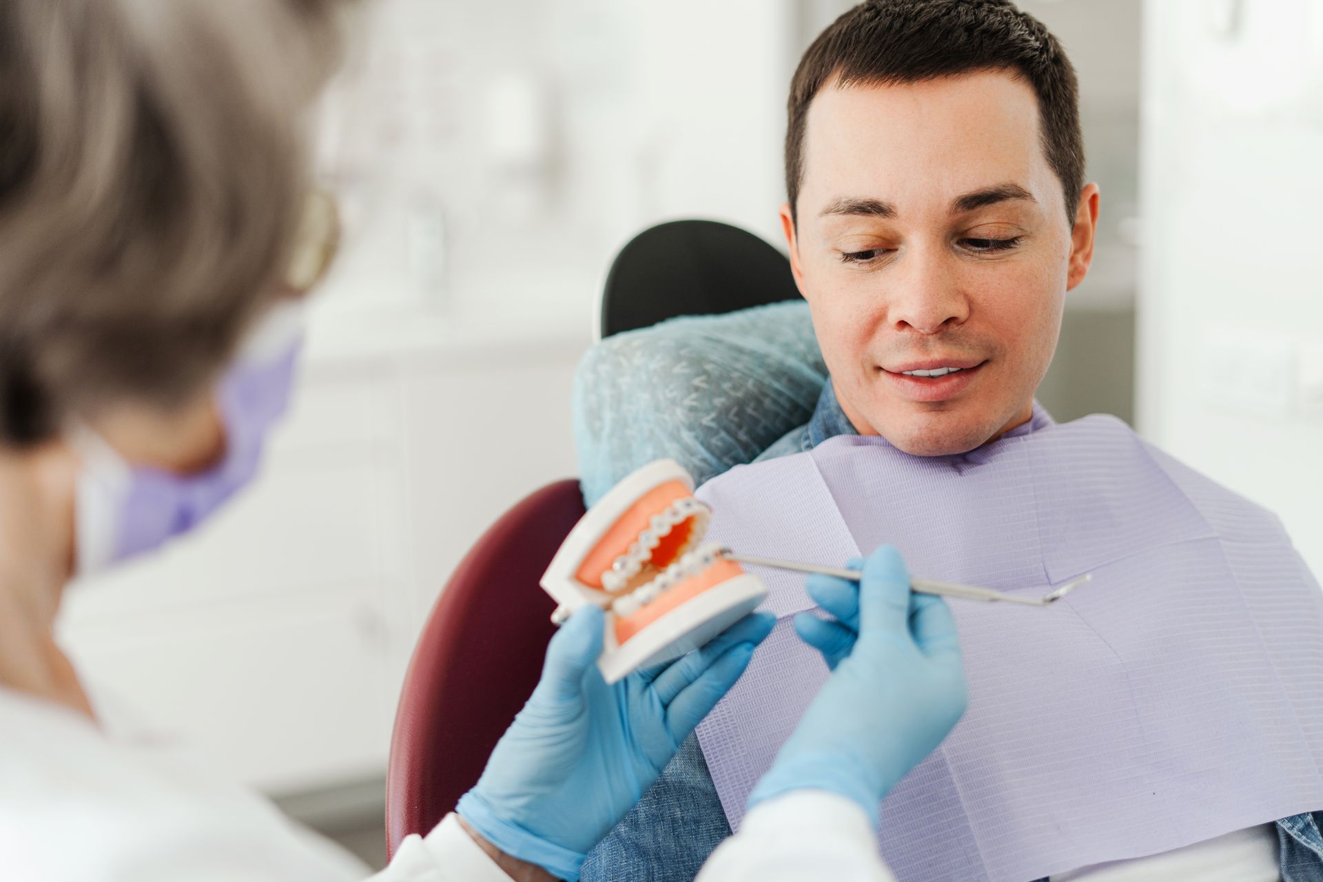 A man is sitting in a dental chair while a dentist examines his teeth.