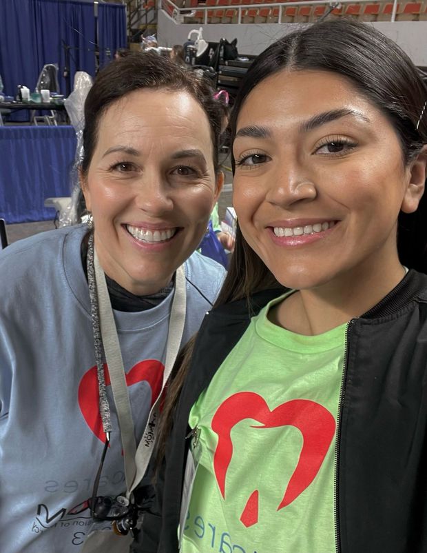 Two women are posing for a picture together and one of them is wearing a green shirt with a heart on it.