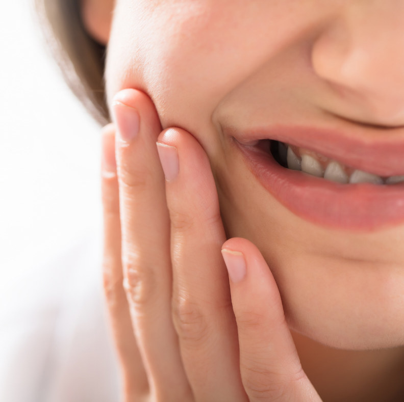 A woman is smiling and touching her face with her hand.