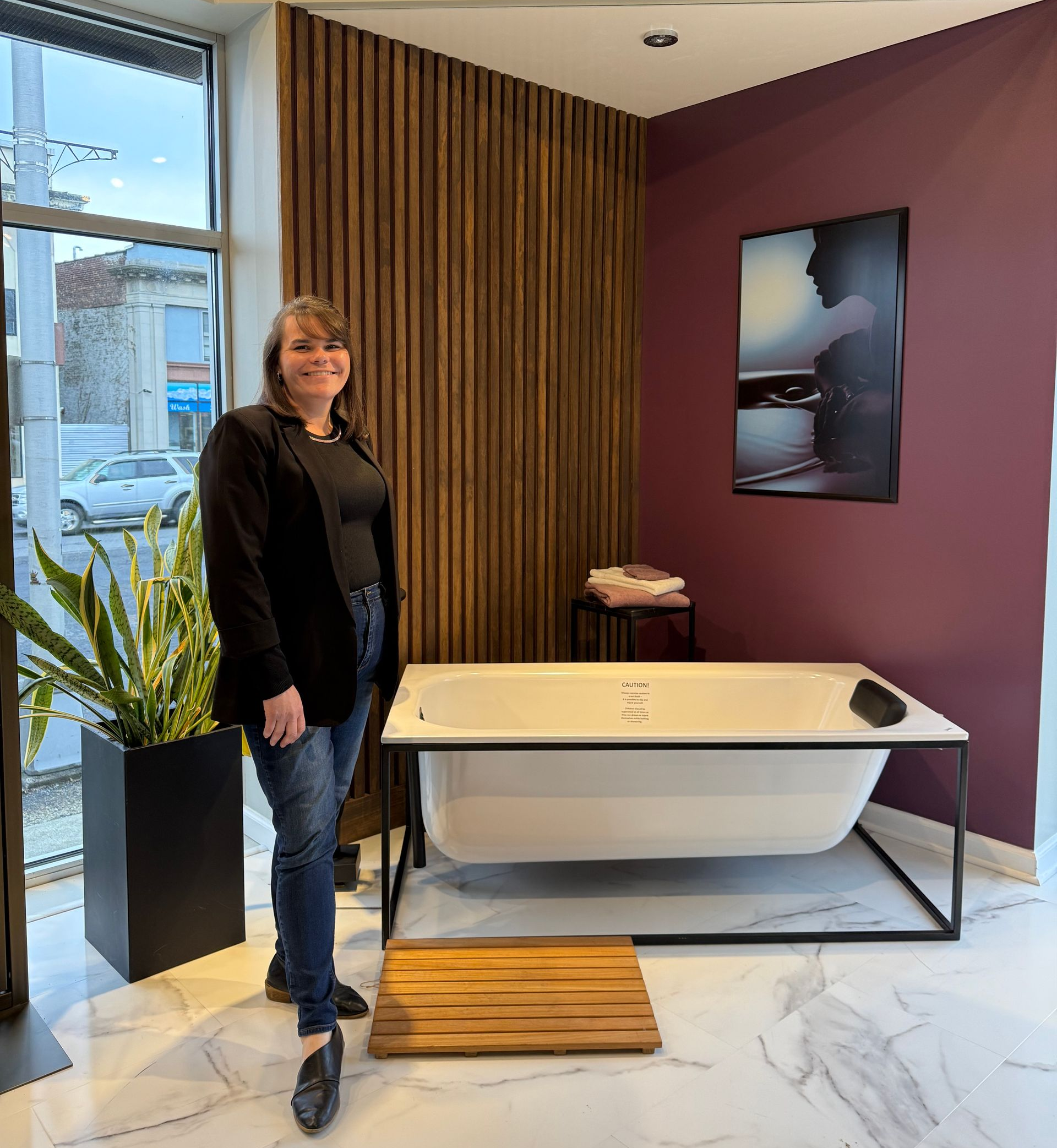 Woman standing near a bathtub in a showroom with wooden accents and a modern aesthetic.