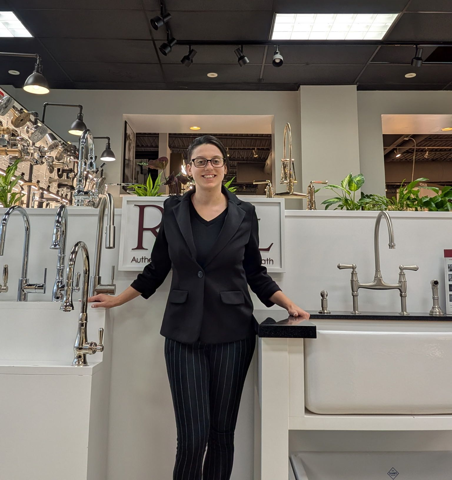 Woman in blazer standing by kitchen faucet displays.