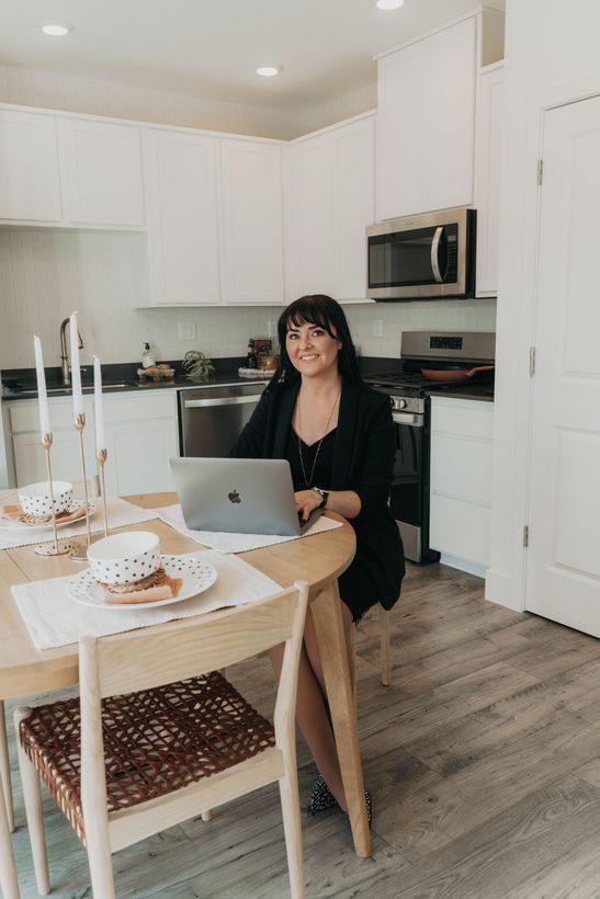 A woman is sitting at a desk with a laptop and a vase of flowers.