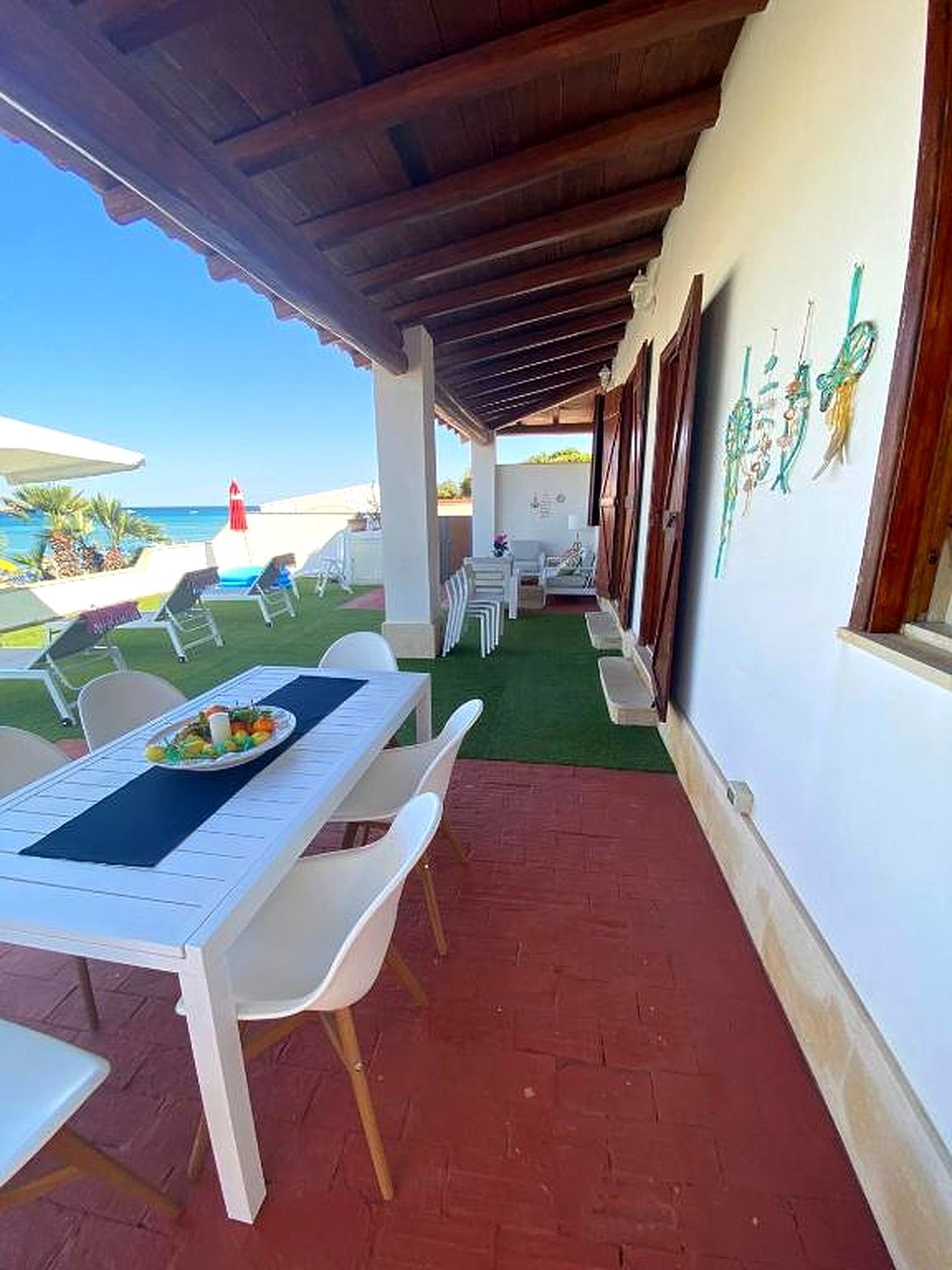 Patio esterno con tavolo bianco, sedie e vista sull'oceano.