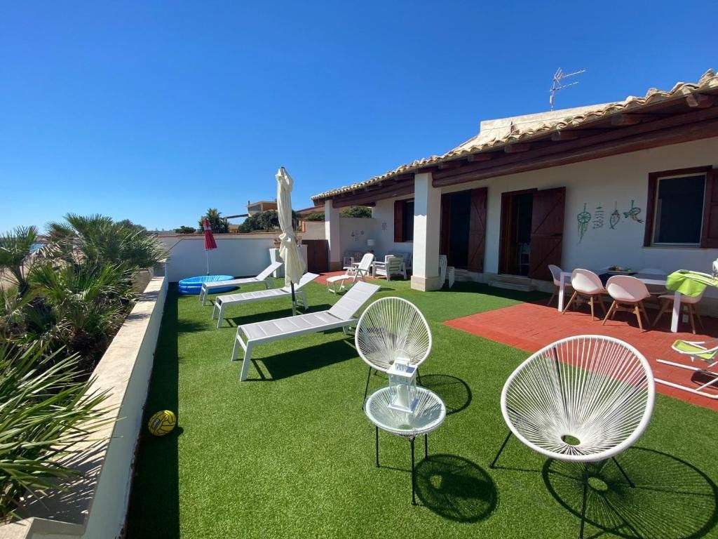 Patio sul tetto con prato verde, sedie a sdraio, tavolino, ombrellone e una casa con porte aperte sotto un cielo azzurro e limpido.