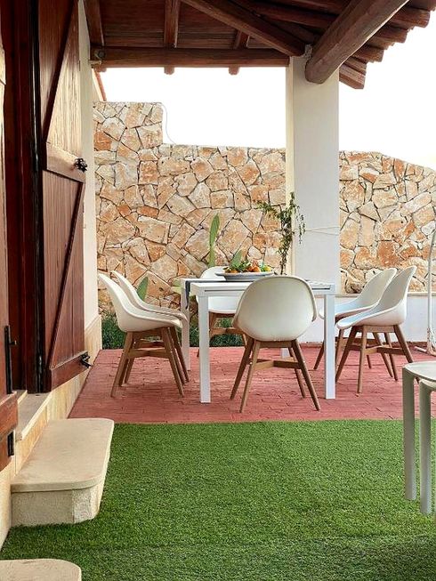 Zona pranzo all'aperto con tavolo bianco, sedie sul patio, muro in pietra e prato verde.