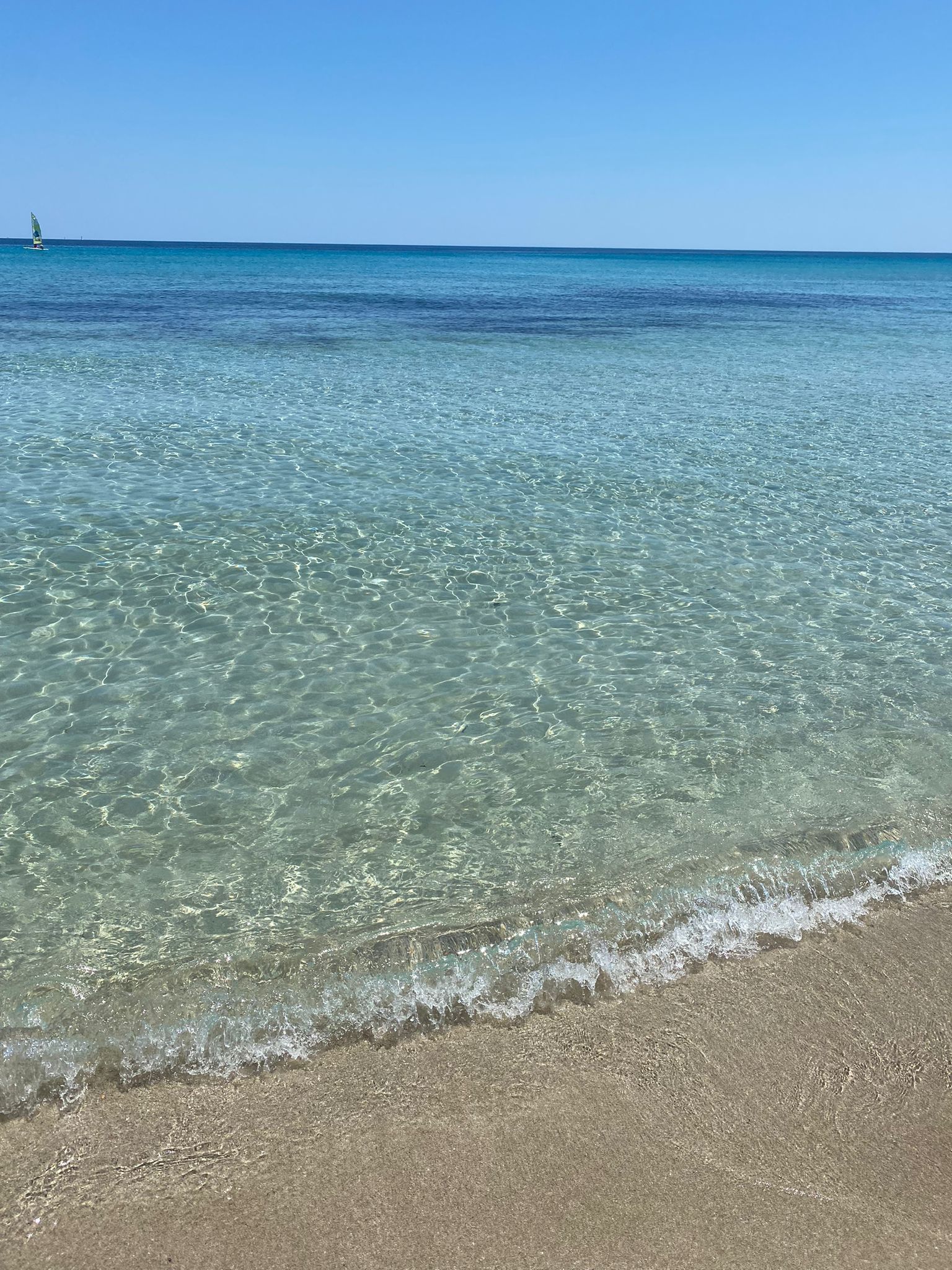 Area lounge con sedie, tavolino, ombrellone e vista sulla spiaggia. Cielo azzurro, oceano ed erba sintetica.