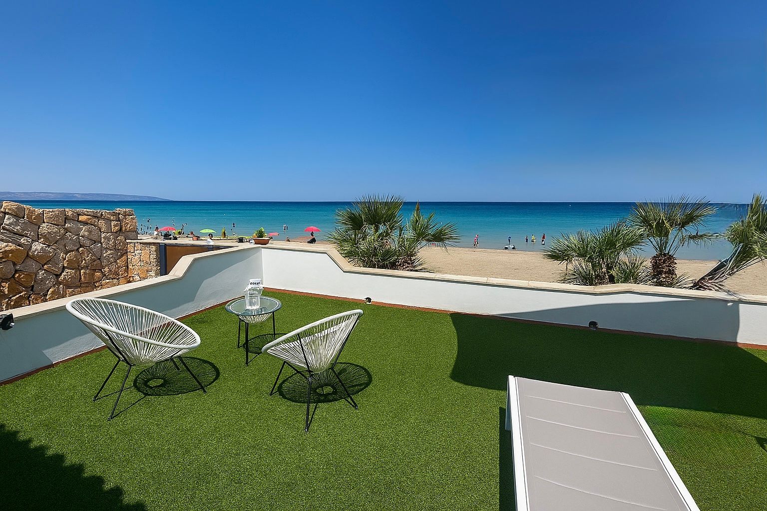 Patio con sedie e vista sulla spiaggia e sull'oceano sotto un cielo azzurro.