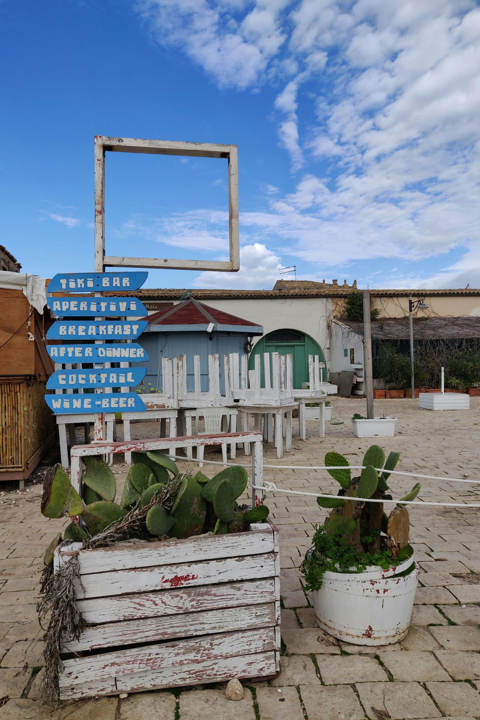 Scena di spiaggia con cartello, tavoli di legno e cactus sullo sfondo di un cielo blu.