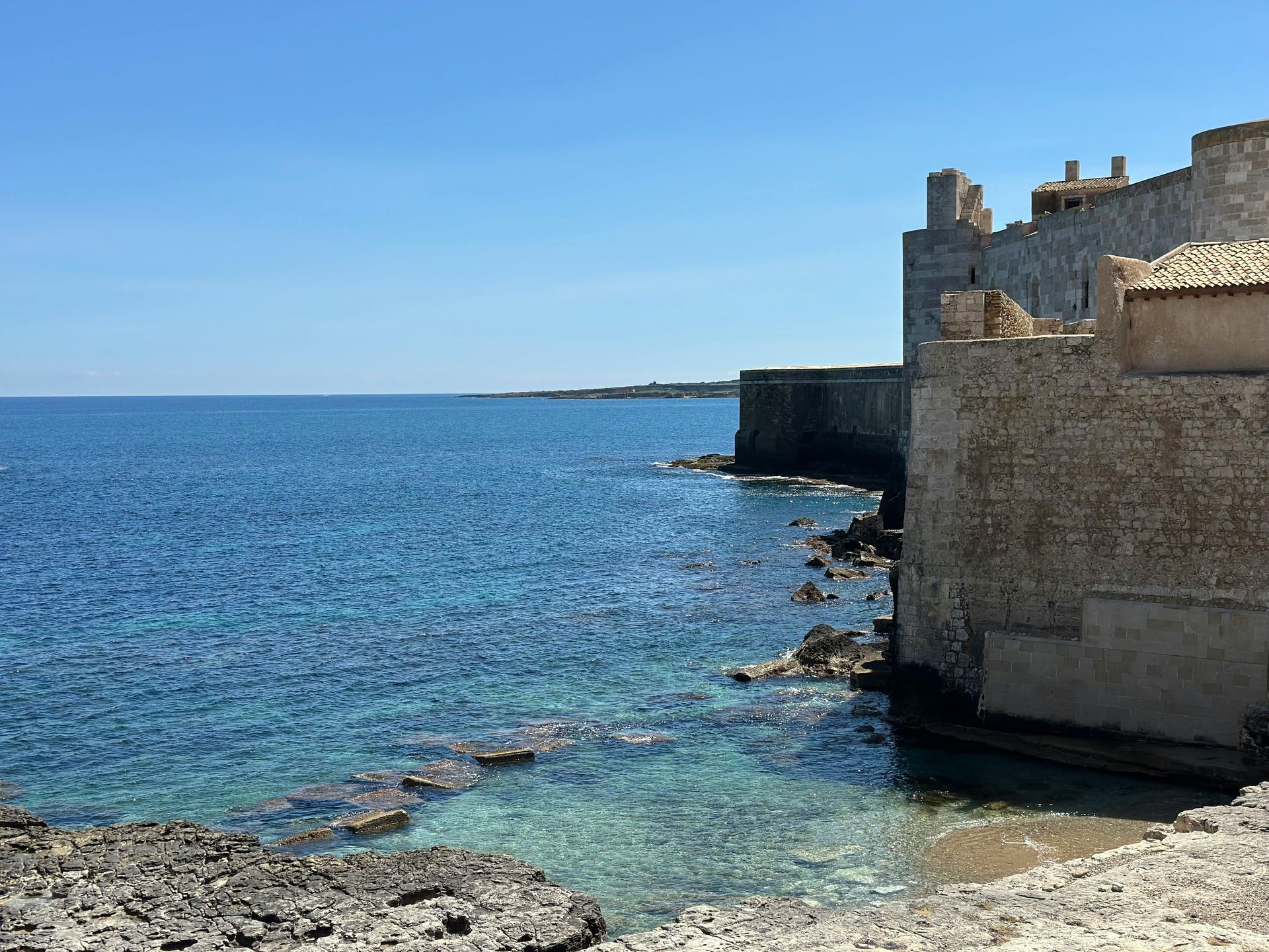 Mura in pietra di un antico forte lungo il blu del Mar Mediterraneo sotto un cielo limpido.