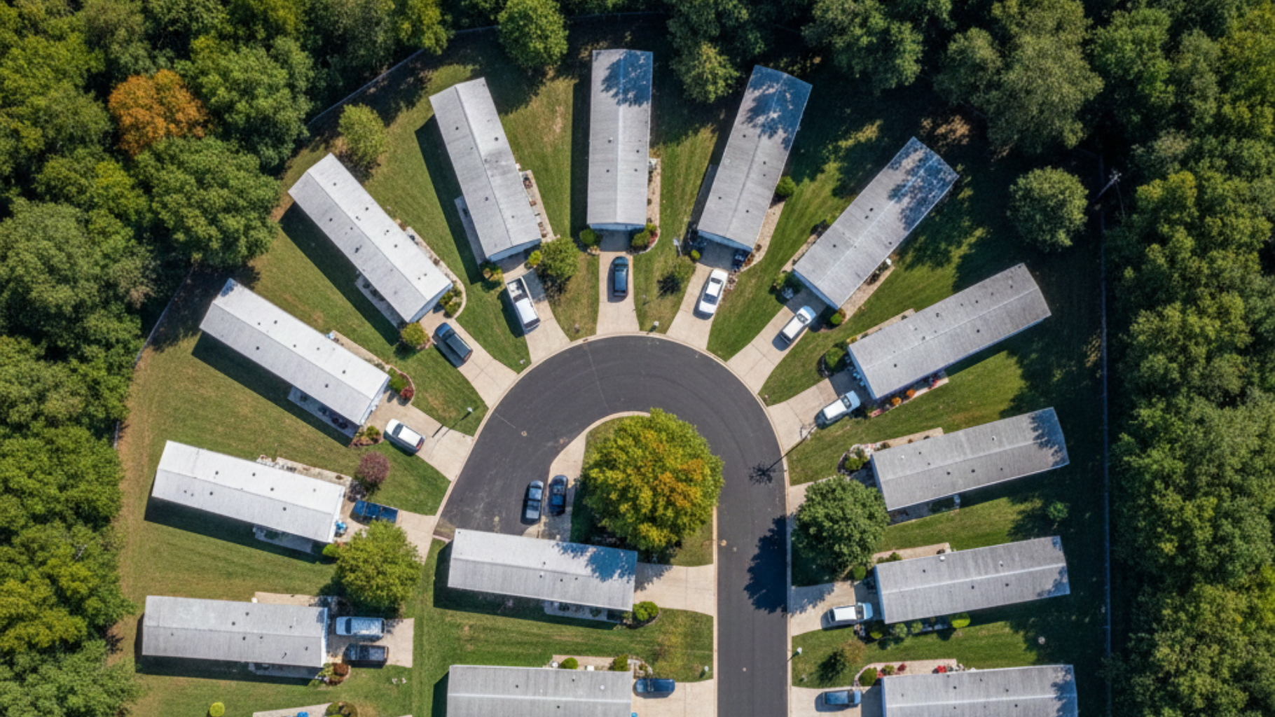 Aerial view of a horseshoe-shaped residential area with identical houses and a central road, surrounded by trees.