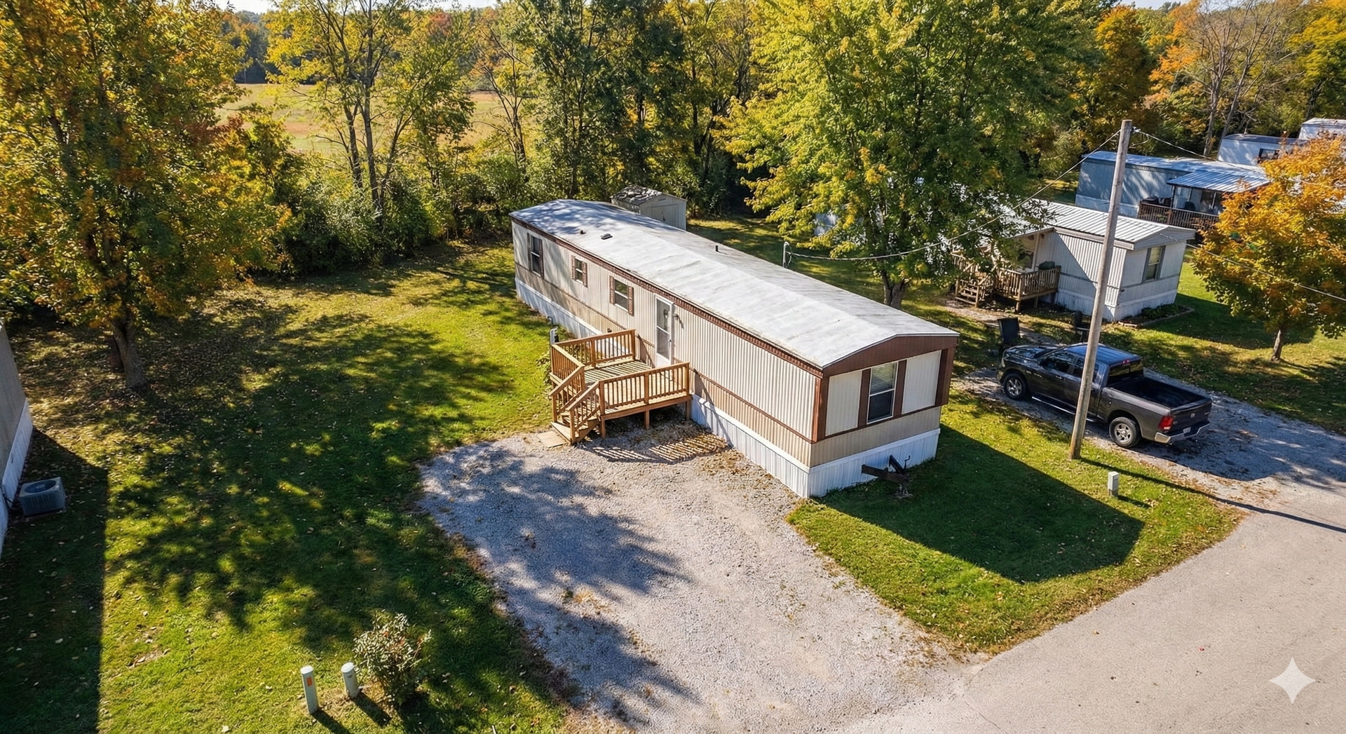 Mobile home in a yard, gravel driveway, wooden steps. Trees and parked truck visible.