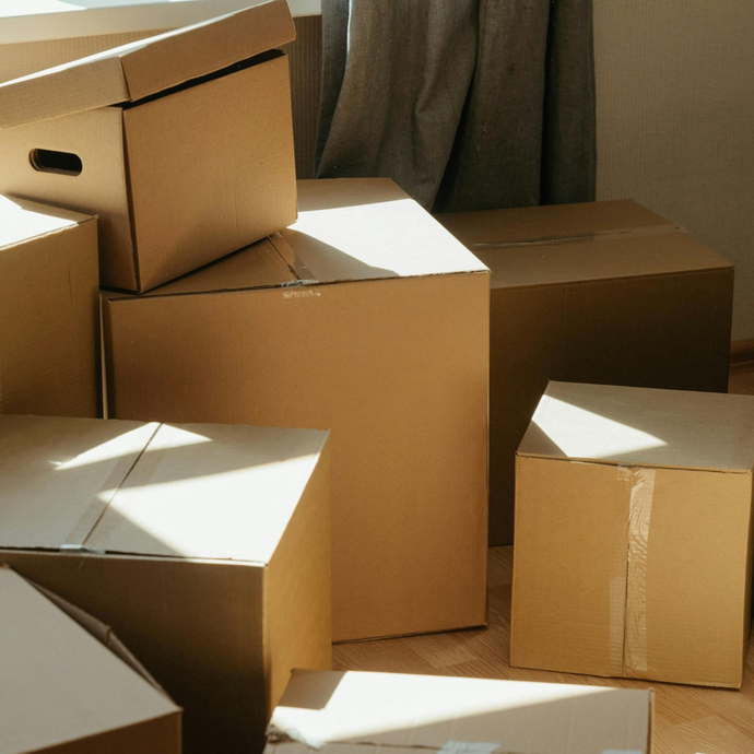 Cardboard moving boxes stacked indoors near a curtain.