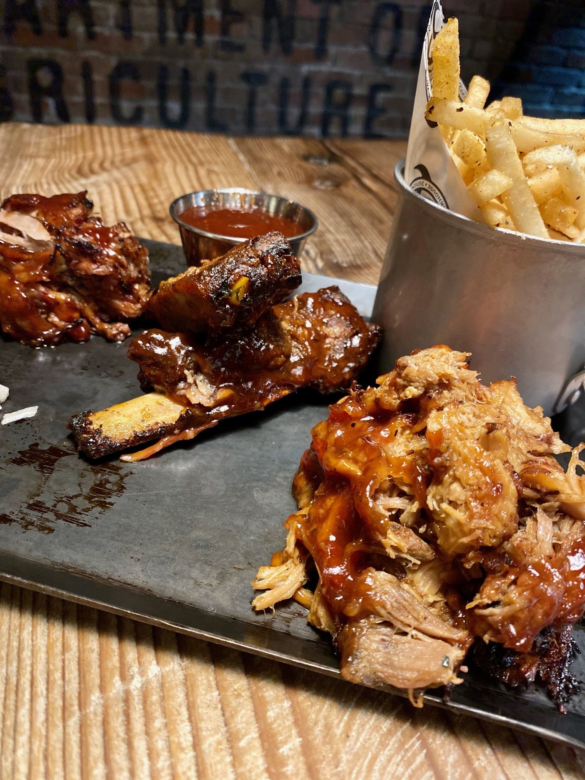 a tray of ribs and pulled pork with a bucket of french fries