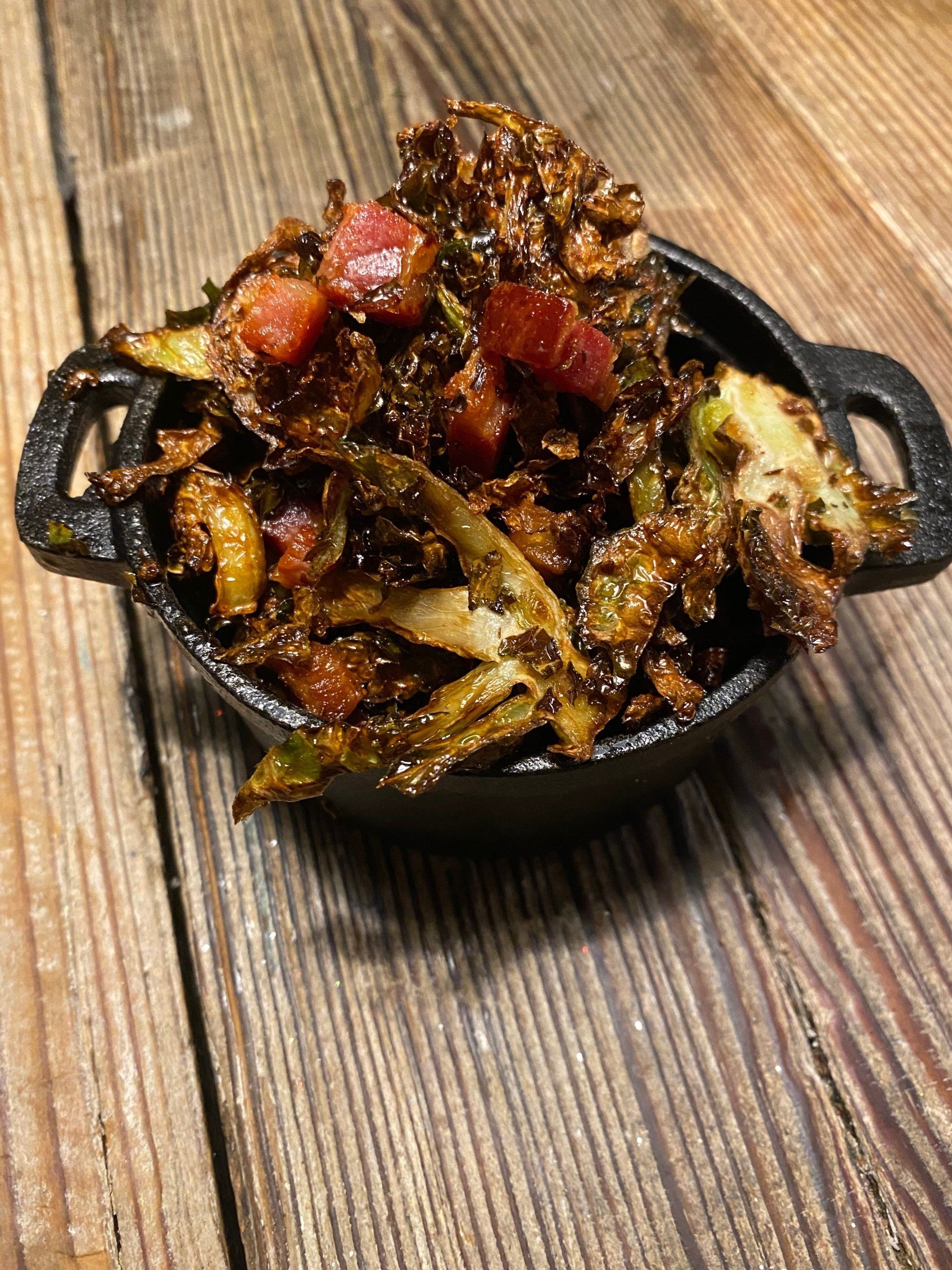 a bowl of food with vegetables and bacon on a wooden table