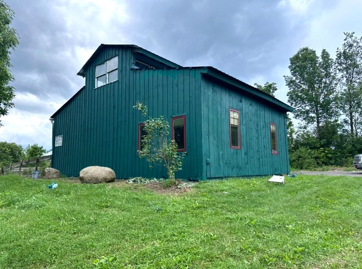 Barn painting services completed by Patrick Farm Painting in Buffalo, New York. This image shows a beautifully restored farm building surrounded by open countryside and fresh landscaping. The siding and exterior surfaces appear clean, professionally coated, and vibrant under natural outdoor lighting. Experienced barn painters from Patrick Farm Painting, the trusted farm painting guy and company that paints barns in New York, carefully transformed this rural structure while preserving its original character. The scene gives visually impaired visitors a vivid sense of the peaceful farm setting, detailed craftsmanship, and the dramatic before-and-after improvement of the barn or farmhouse exterior.