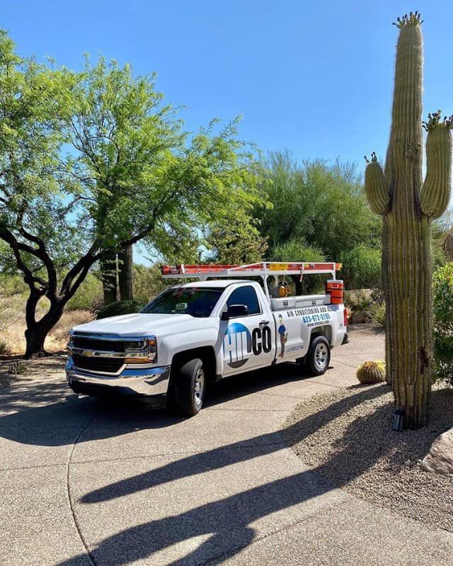 White work truck parked on a driveway with a saguaro cactus in the background. Blue sky and sunny day.