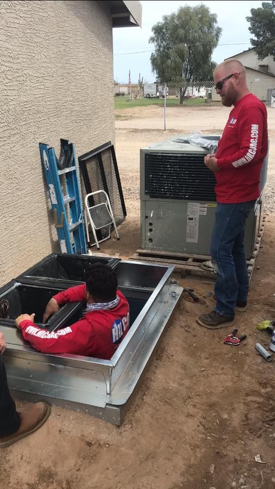 A technician wearing a mask working on a furnace in an attic.