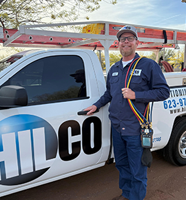 HVAC technician beside a truck, holding gauges. Blue uniform, white truck, logo
