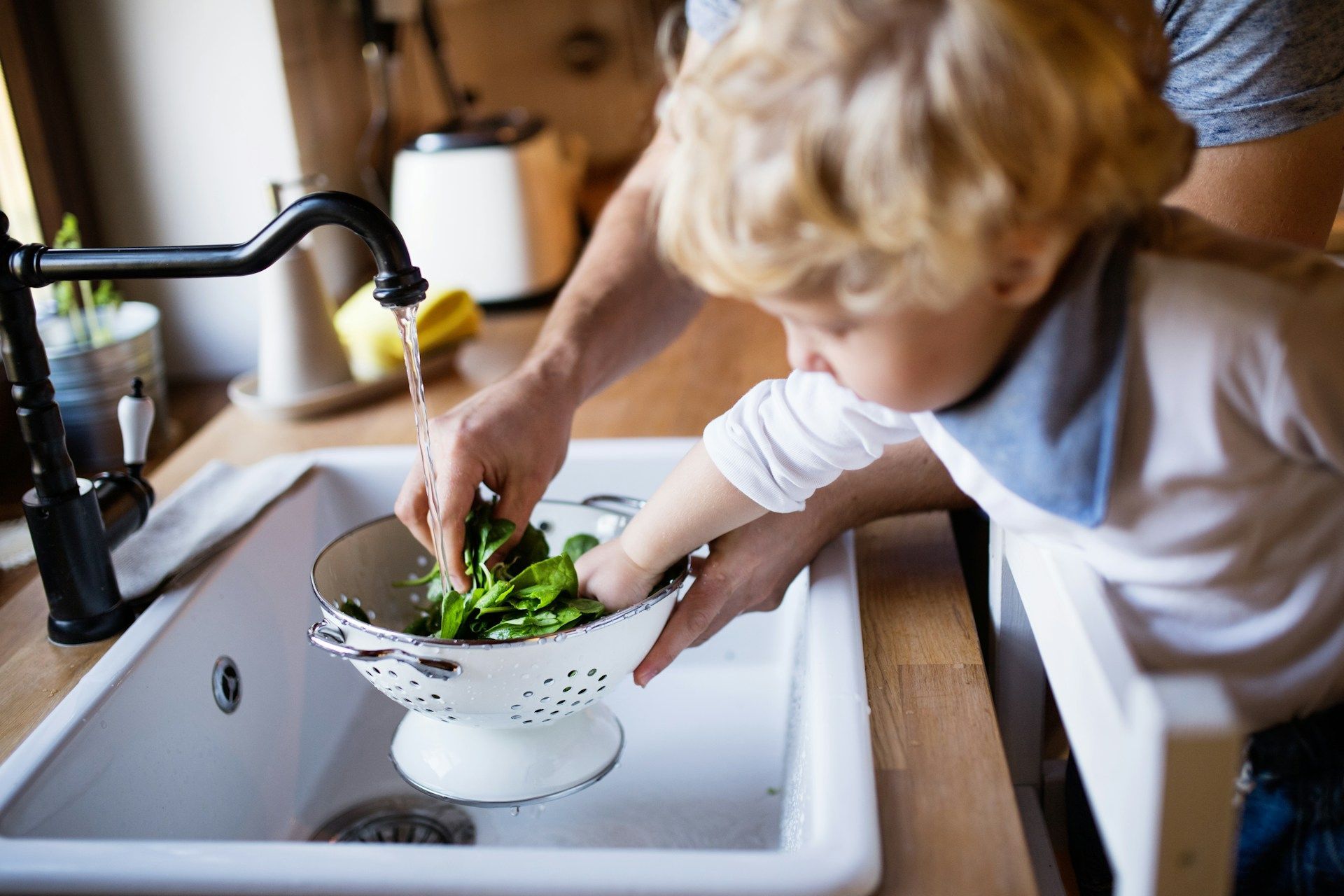 A person and a child washing greens in a kitchen sink.