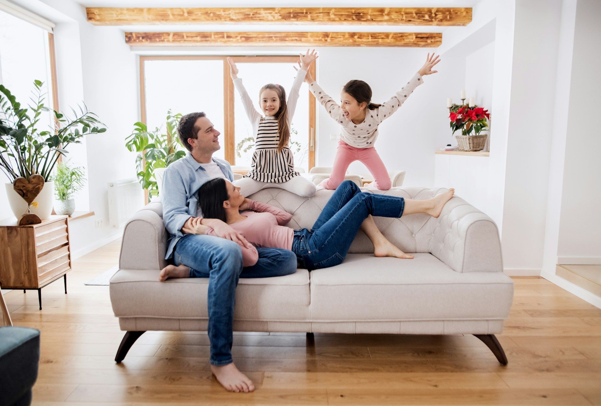 Family on a sofa with two children jumping up. Living room with plants.