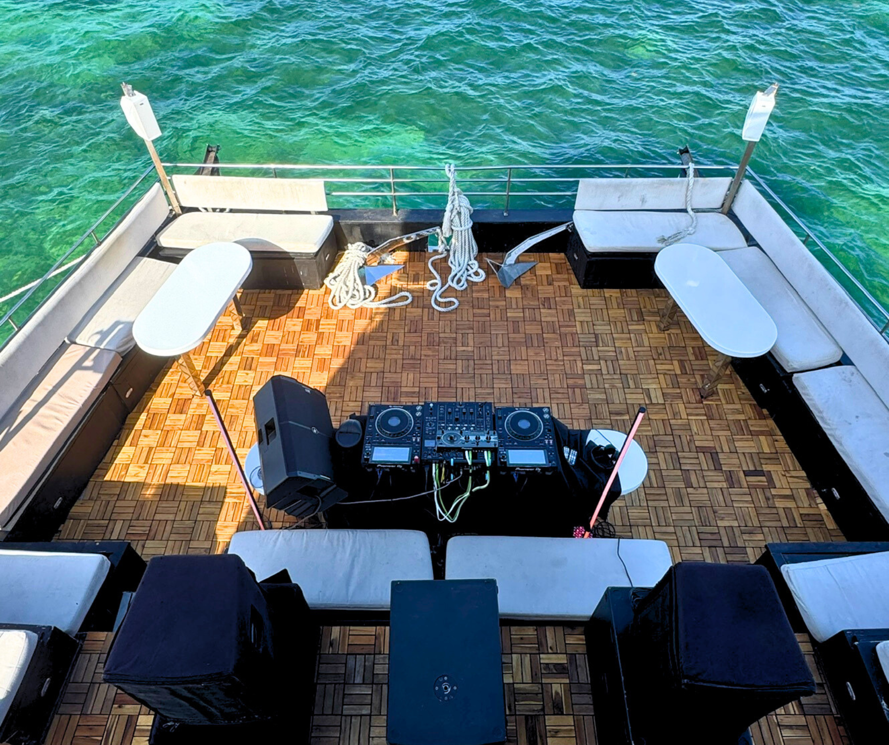 Instalación de DJ en la cubierta de un barco de fiesta, rodeado de asientos, en agua turquesa clara. .Hix stage
