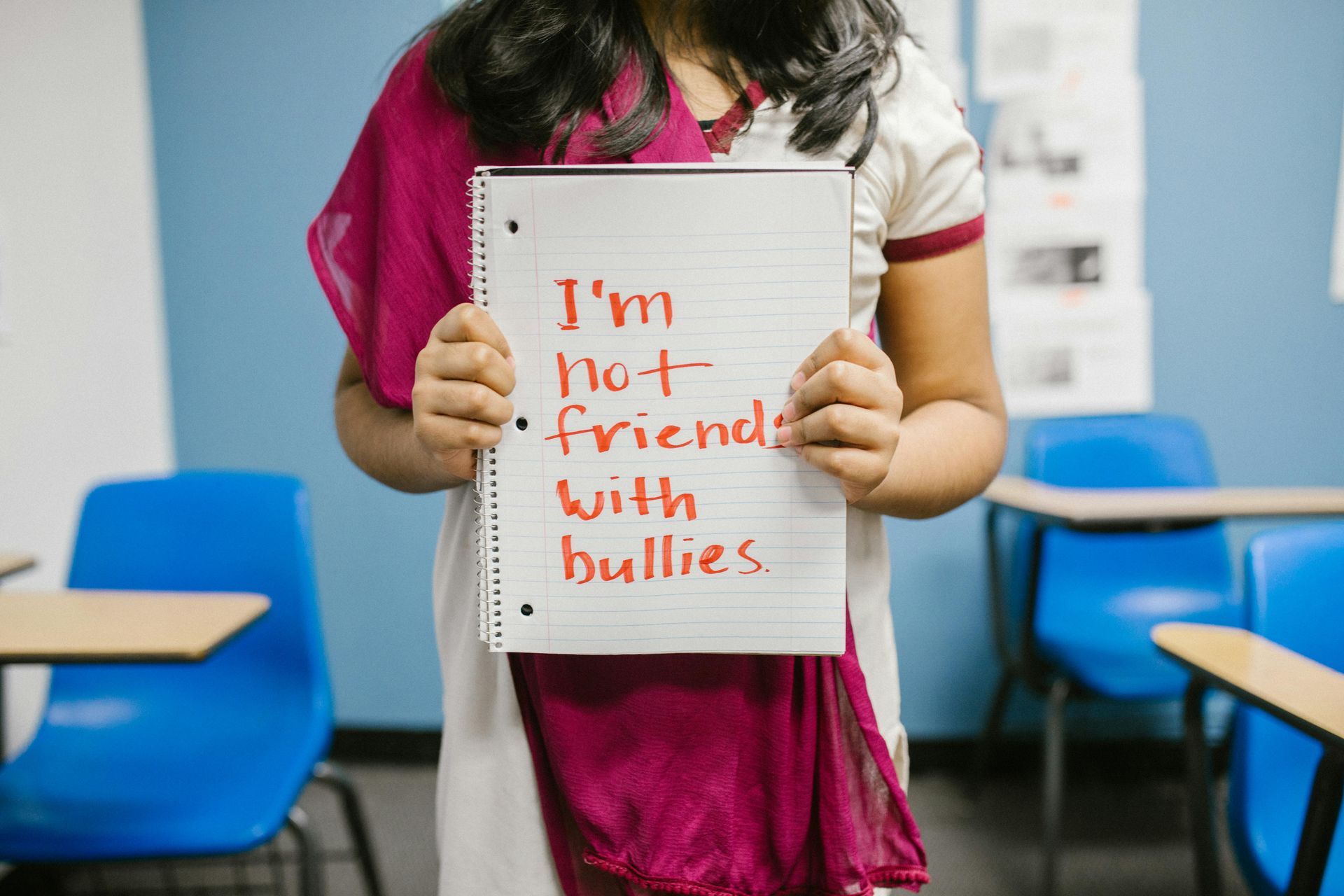 A person holding a notebook that says, “I’m not friends with bullies,” in a classroom.