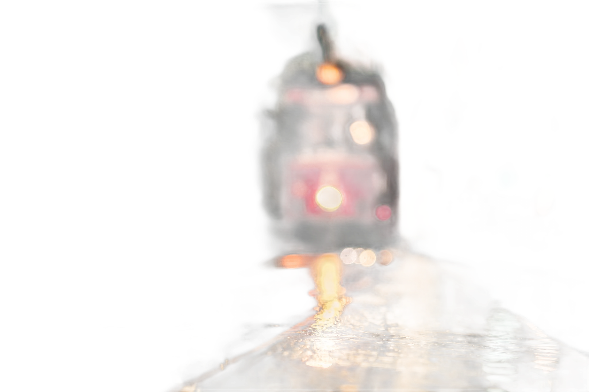 Street view, blurry red tram with headlights on, reflected in wet pavement at dusk.