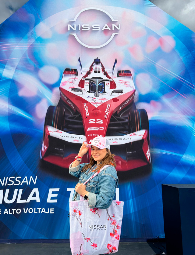 Woman posing with Nissan Formula E car. Holding tote bag and wearing a cap with cherry blossom designs.