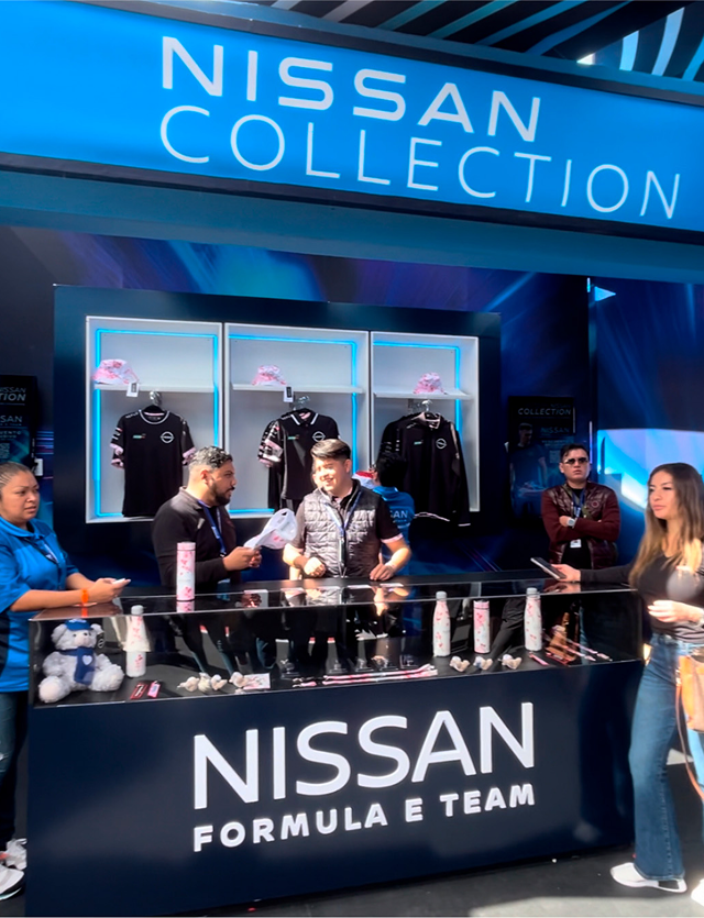 Nissan Formula E Team merchandise display, people interacting, blue and black branding.