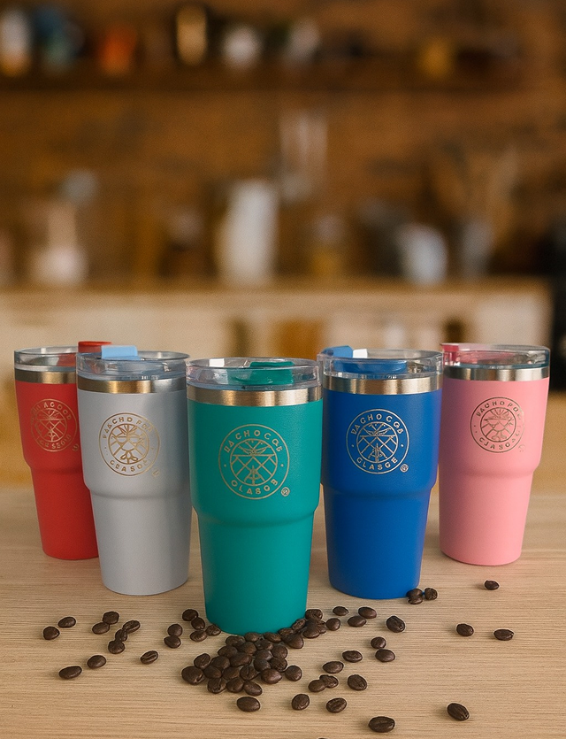 Five colorful insulated tumblers with gold emblems, on a wooden table with scattered coffee beans.