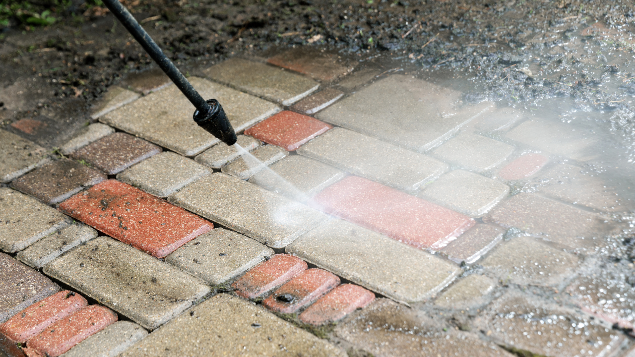 Pressure washer cleaning a dirty brick patio, spraying water across red and gray pavers