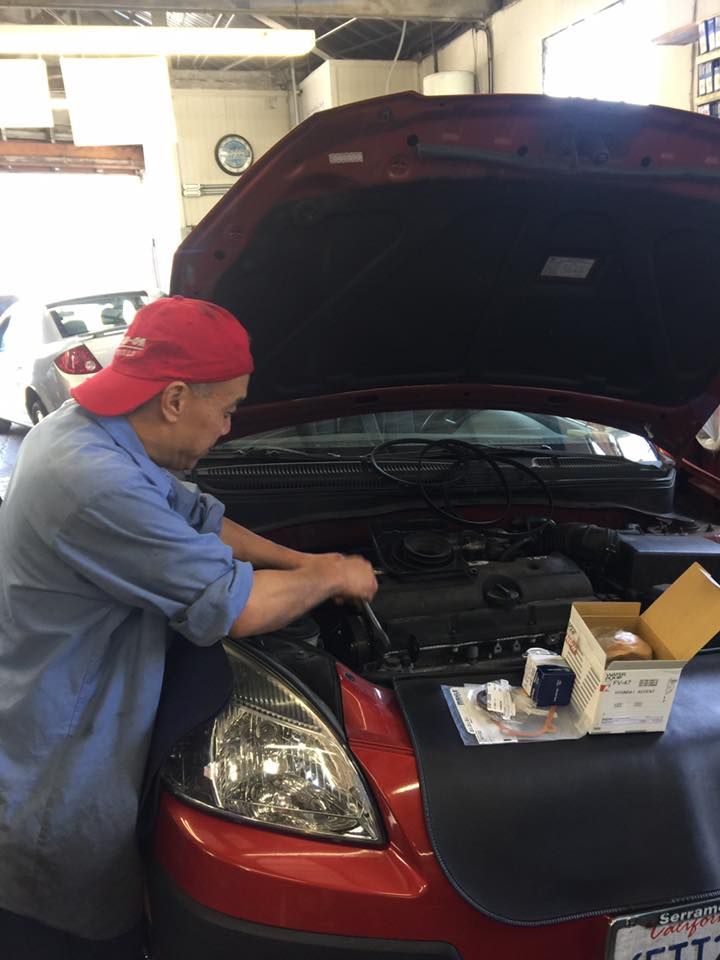 Mechanic in red cap working on red car engine in garage. | Pacifica Auto Works