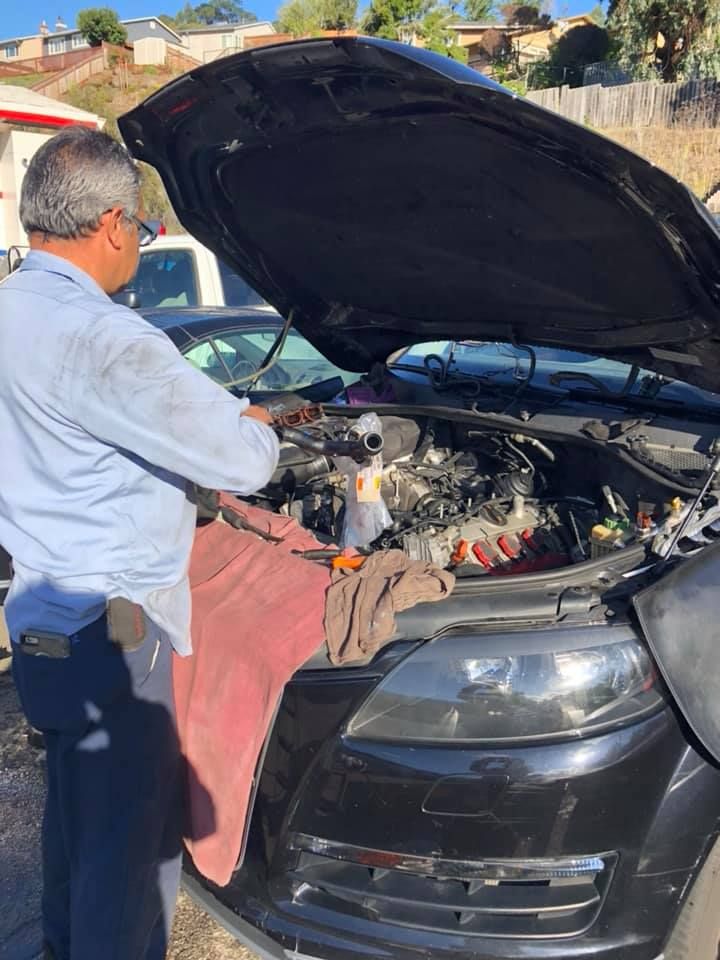 Mechanic working on a black car with the hood open outdoors on a sunny day. | Pacifica Auto Works