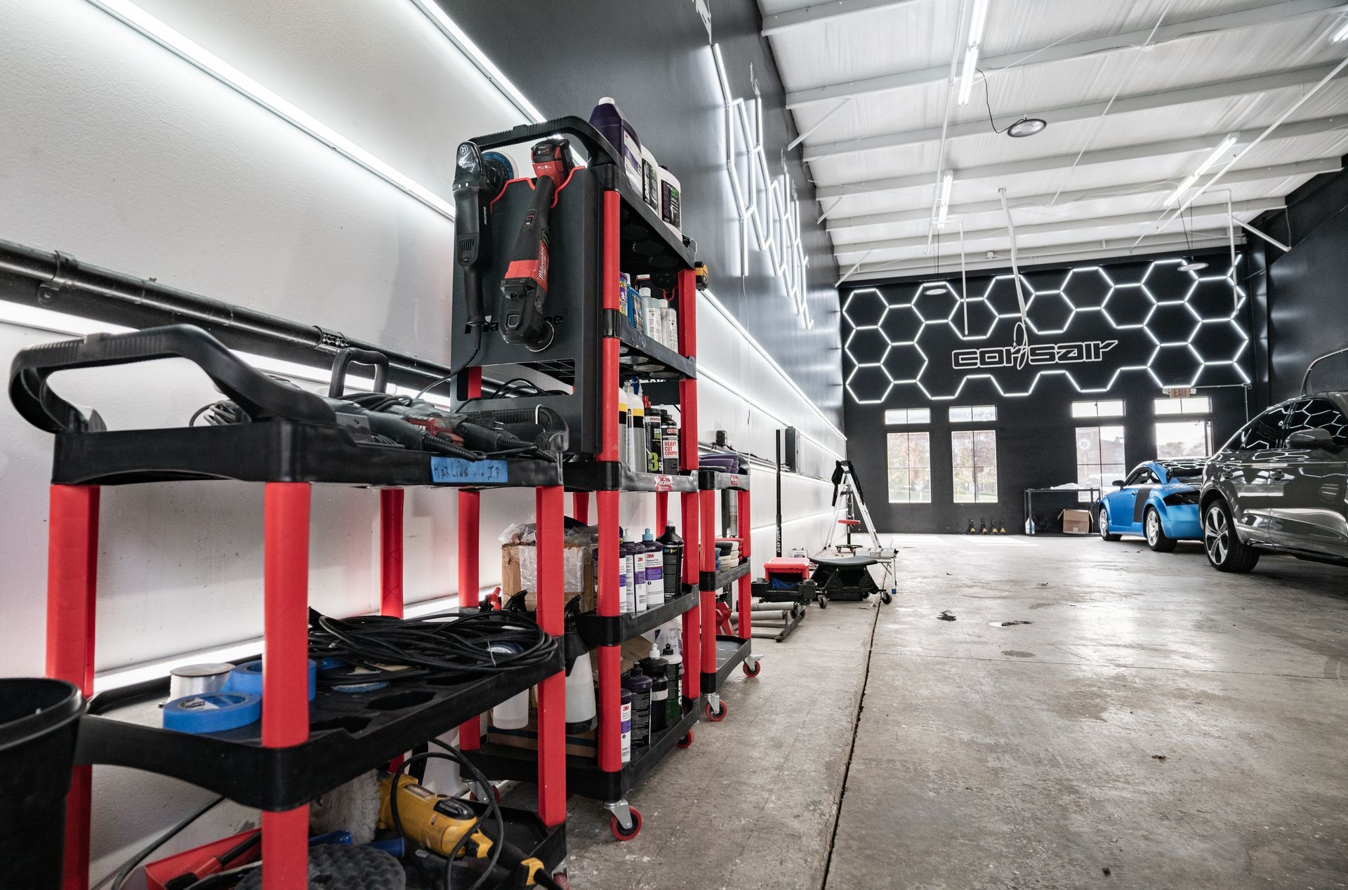 A garage with a lot of tools on shelves and a car in the background.