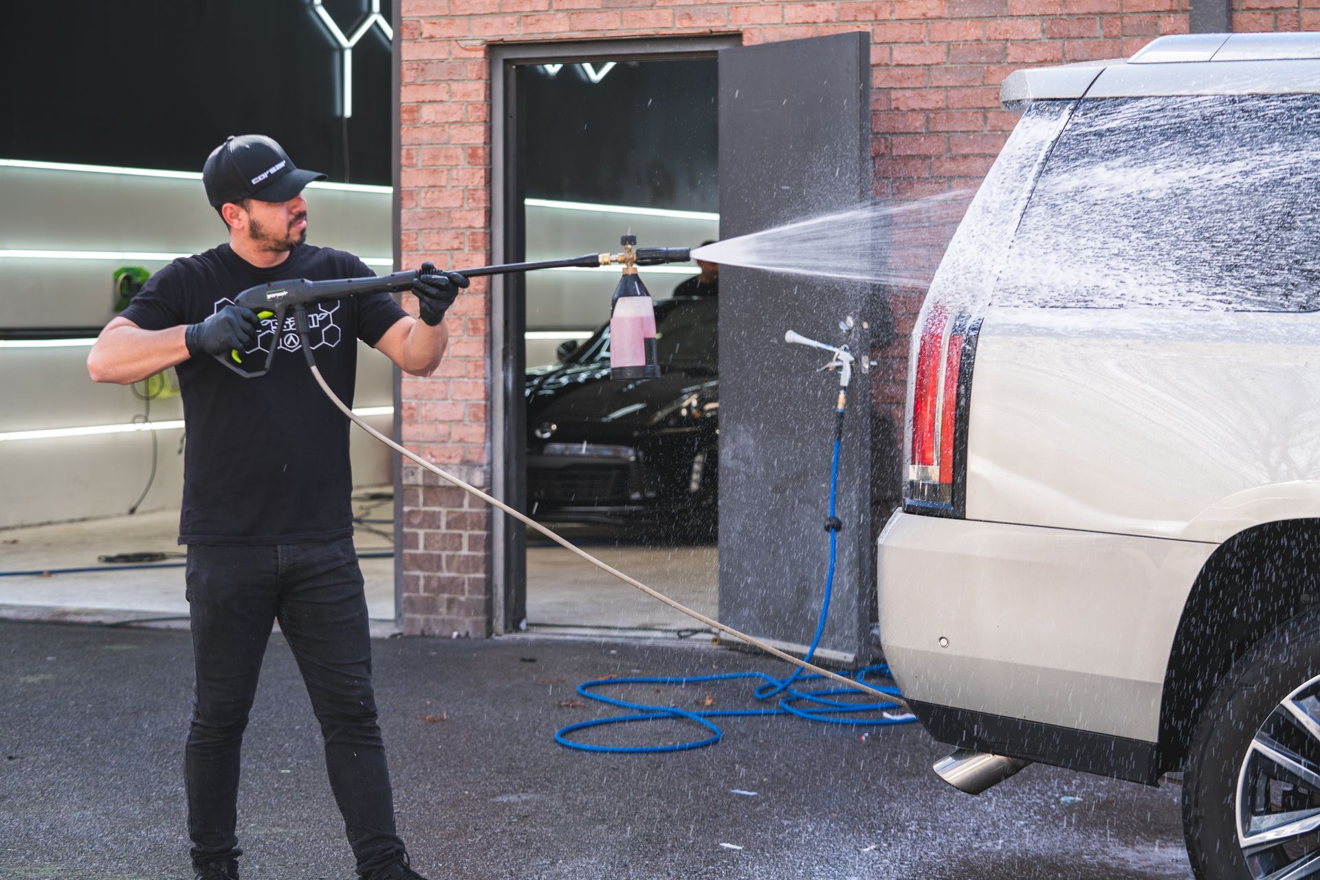 A man is washing a white suv with a high pressure washer.