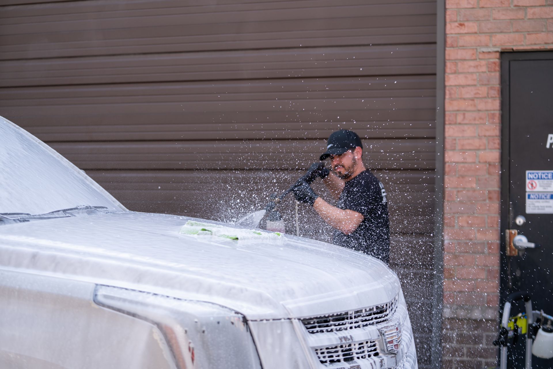 A man is washing a white truck with a high pressure washer.